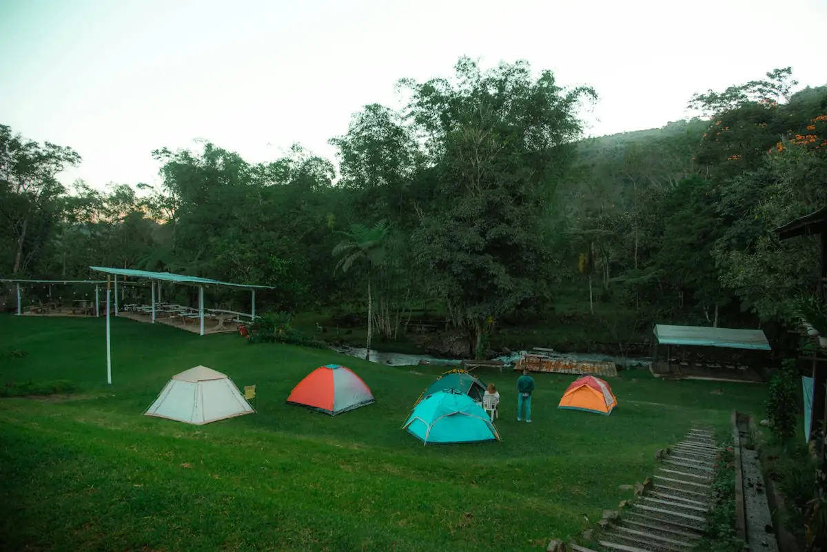 Beberapa tenda berdiri di atas rumput hijau dikelilingi pepohonan tropis